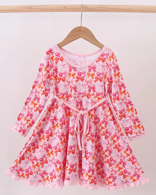 Pink floral dress with long sleeves on a wooden hanger against a white background
