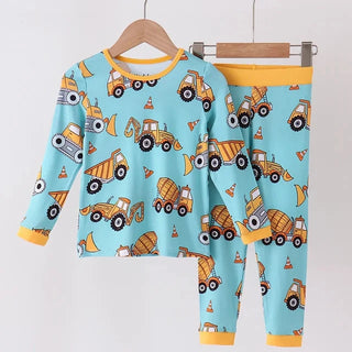A two-piece children's pajama set hanging on wooden hangers against a plain light background. The set includes a long-sleeve top and matching pants in light blue with a playful print of yellow construction vehicles, including dump trucks, excavators, and cement mixers, plus yellow trim at the collar, cuffs, and hem.