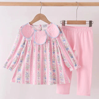 A toddler girl's two-piece clothing set hanging on wooden hangers against a plain white wall. The set includes a long-sleeve blouse with a pink floral and vertical stripe pattern and a large pink Peter Pan collar, paired with solid light pink pants.