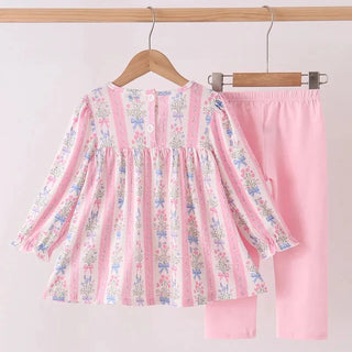 A children's two-piece clothing set hanging on wooden hangers against a light pink background. The set includes a long-sleeve top with vertical pink stripes and a delicate multicolor floral print, paired with solid light pink pants.