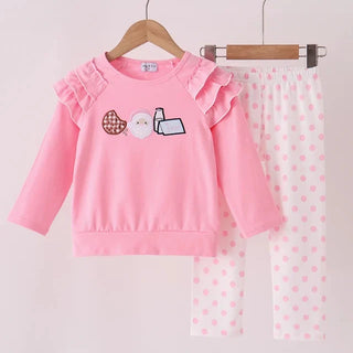 A children's two-piece clothing set hanging on wooden hangers against a plain light background. The set includes a pink long-sleeve top with ruffled shoulders and a cute graphic on the chest, paired with white leggings featuring pink polka dots.