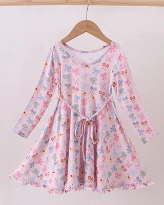 Pink dress with colorful bow pattern on a wooden hanger against a white background