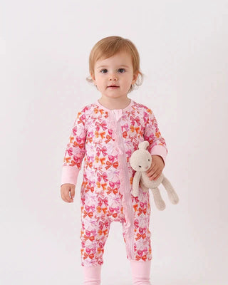 Baby in a pink floral onesie holding a teddy bear on a white background