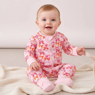 Baby in a pink floral outfit sitting on a wooden floor.