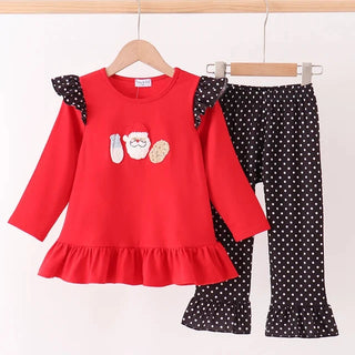 A toddler girl's two-piece clothing set hanging on wooden hangers against a plain white wall. The set includes a bright red long-sleeve top with black polka-dot ruffled shoulder panels, a Santa Claus graphic on the chest, and a matching pair of black polka-dot pants with ruffled hems.
