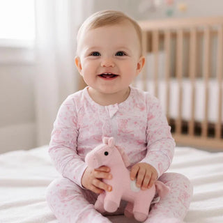 Baby in pink pajamas holding a pink toy in a nursery