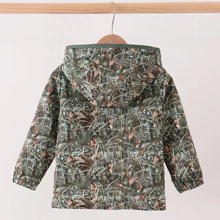 A hooded children's jacket with a green and brown marshland camouflage pattern, hanging on a wooden hanger from a light wood rod against a plain off-white background.