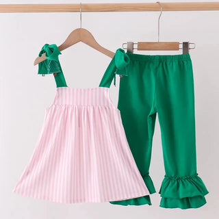 A toddler girl's two-piece outfit hanging on wooden hangers against a plain white wall. The set includes a sleeveless dress with light pink and white vertical stripes and green ruffled shoulder ties, paired with matching solid green ruffled capri pants.