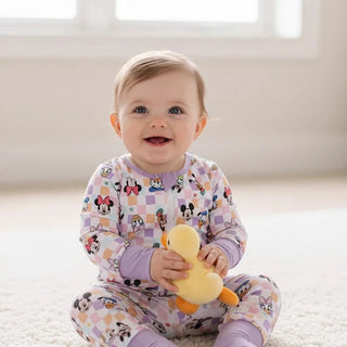 Baby sitting on a carpeted floor holding a toy, wearing colorful pajamas.