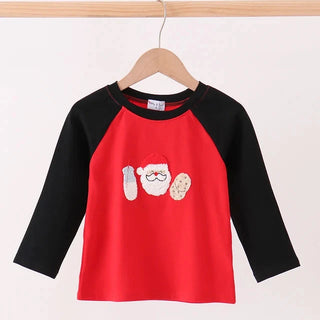 A children's long-sleeve raglan top hanging on a wooden hanger, featuring a bright red body and black sleeves, with a festive Santa Claus graphic on the chest.