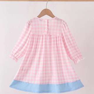 A pink and white gingham long-sleeve dress with a light blue hem, hanging on a wooden hanger against a plain light background.