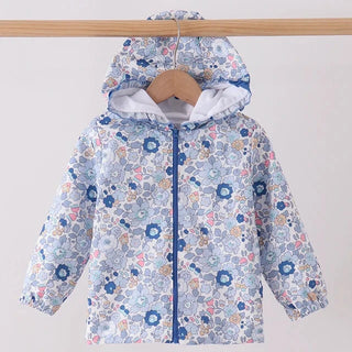 A children's hooded jacket with a light blue background and a dense floral print in blue, pink, and yellow, hanging on a wooden hanger from a wooden clothes rack.