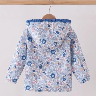 A children's hooded jacket with a blue floral pattern, hanging on a wooden hanger from a light wood clothing rack against a plain light gray wall.