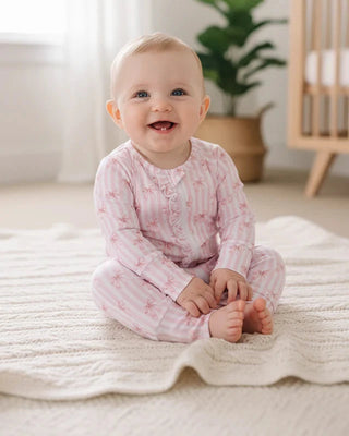 Baby sitting on a blanket in a nursery with a plant and crib in the background