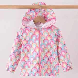 A children's hooded zip-up jacket with a pastel rainbow arch pattern, hanging on a wooden hanger from a wooden clothes rail against a plain light background.
