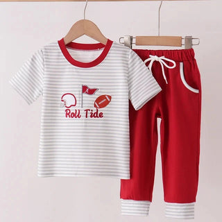 A two-piece children's outfit set hanging on wooden hangers from a wooden rod. The set includes a white short-sleeve t-shirt with thin gray horizontal stripes, a red collar, and a red 'Roll Tide' football graphic on the front, paired with red sweatpants featuring a white drawstring waist, white pocket trim, and striped gray cuffs.