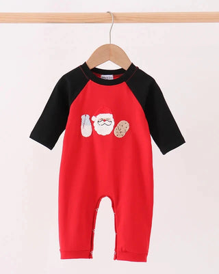 A baby long-sleeve romper in red and black, hanging on a wooden hanger. The red body features a graphic of Santa Claus's face with a white beard and a cookie on the chest.