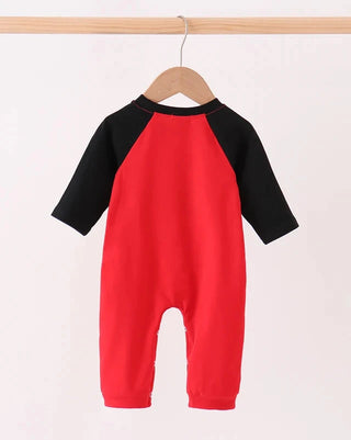 A baby one-piece romper hanging on a wooden hanger, featuring a bright red body and black raglan sleeves, set against a plain white background.