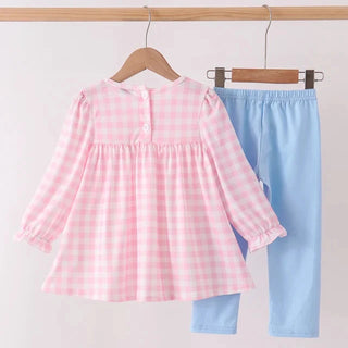 A toddler girl's two-piece clothing set hanging on wooden hangers against a plain white wall. The set includes a pink and white gingham long-sleeve top with a buttoned neckline and ruffled cuffs, paired with light blue pants.