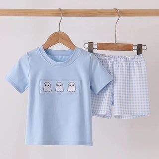 A children's two-piece outfit set hanging on wooden hangers against a plain light background. The set includes a light blue short-sleeve T-shirt with three small white ghost graphics on the chest, and matching light blue-and-white gingham shorts.