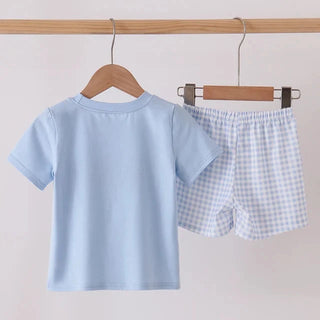 A two-piece children's outfit set hanging on wooden hangers from a wooden rod. The set includes a light blue short-sleeve t-shirt and matching light blue and white gingham check shorts.