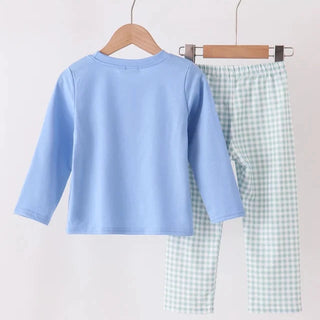 A two-piece children's outfit hanging on wooden hangers against a plain light background. The set includes a light blue long-sleeve top and light green and white gingham pants.