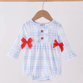 A baby girl's long-sleeve romper in a light blue and white gingham pattern, featuring red fabric bows on the sleeves, three brown buttons on the chest, and a ruffled neckline, hanging on a wooden hanger against a plain light background.