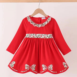 A red long-sleeve dress with floral embroidery on the collar, waistband, and hem, hanging on a wooden hanger against a light beige background.