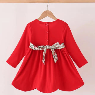 A bright red long-sleeve dress hanging on a wooden hanger against a plain light background. The back of the dress has three small buttons and is cinched at the waist with a patterned fabric bow featuring green, white, and red tones.