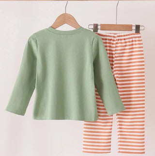 A children's two-piece outfit hanging on wooden hangers from a wooden rod. The set includes a sage green long-sleeve top and orange-and-white striped pants.