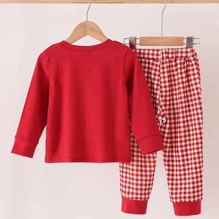A children's two-piece outfit set hanging on wooden hangers from a light wood rod. The set includes a solid bright red long-sleeve top and matching red-and-white gingham checkered pants with solid red cuffs.