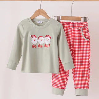 A two-piece children's outfit hanging on wooden hangers against a plain light background. The set includes a sage green long-sleeve top with three Santa Claus faces and 'ho ho ho!' text on the front, and red-and-white gingham pants with a solid sage green cuff.