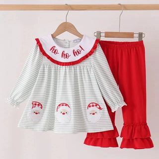 A toddler girl's Christmas-themed two-piece outfit hanging on wooden hangers against a light pink wall. The set includes a white and light green striped long-sleeve top with a red ruffled collar embroidered with 'ho ho ho!', and matching solid red ruffled pants.