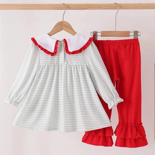 A toddler girl's two-piece outfit hanging on wooden hangers against a light pink background. The set includes a long-sleeve top with white and light green stripes, a white collar with red ruffle trim, and matching red ruffled pants.