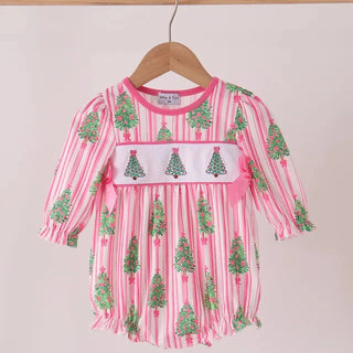 A pink and white striped baby dress with green Christmas tree prints, featuring a white smocked chest panel with green trees and a pink bow, hanging on a wooden hanger.