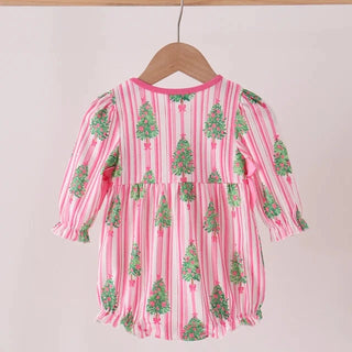 A pink and white vertically striped baby dress with green Christmas tree prints, hanging on a wooden hanger from a light wood rod against a plain off-white wall.