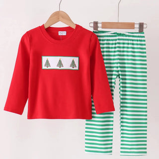 A children's two-piece outfit set hanging on wooden hangers against a plain light background. The set includes a bright red long-sleeve top with a white chest panel featuring three small Christmas tree illustrations, and green-and-white horizontally striped pants.