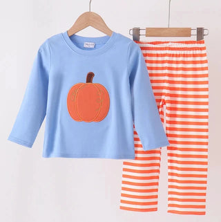 A children's two-piece outfit hanging on wooden hangers against a plain light background. The set includes a light blue long-sleeve top with an orange pumpkin graphic on the front and orange-and-white horizontally striped pants.