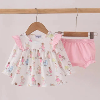 A baby girl's two-piece outfit hanging on wooden hangers against a light pink wall. The set includes a white long-sleeve top with pink ruffle sleeves and a colorful print of cartoon ballerinas, paired with solid light pink bloomers.