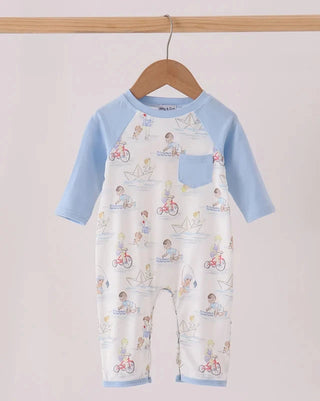 A baby one-piece jumpsuit hanging on a wooden hanger, featuring light blue raglan sleeves and leg cuffs, with a white body covered in a colorful cartoon bicycle and sailboat print. The jumpsuit has a left chest pocket and is displayed against a light pink background.