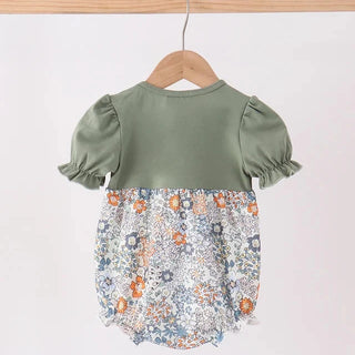 A baby girl's short-sleeve romper hanging on a wooden hanger. The top half is a solid sage green, and the bottom half features a dense, multicolor floral print with blue, orange, and white tones.