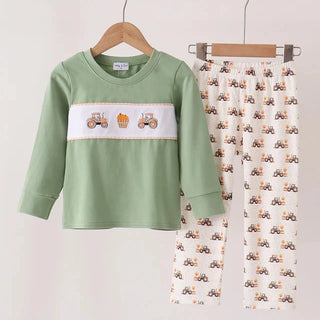 A children's two-piece outfit set hanging on wooden hangers against a plain light background. The set includes a sage green long-sleeve top with a white chest panel featuring embroidered tractors, and cream-colored pants with an all-over small tractor print.