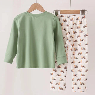 A children's two-piece outfit set hanging on wooden hangers against a plain light background. The set includes a sage green long-sleeve top and white pants with a repeating brown and orange tractor print.