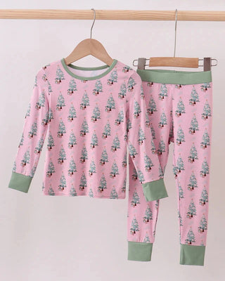 Children's pajama set with tree pattern on pink fabric, hanging on a wooden rod.