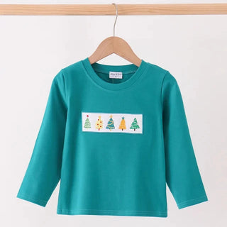 A teal green long-sleeve boys top hanging on a wooden hanger against a plain white wall. The shirt features a white rectangular chest graphic depicting four colorful Christmas trees.