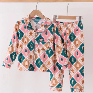 A two-piece children's pajama set hanging on wooden hangers against a plain white wall. The set includes a long-sleeve button-front top and matching pants, both featuring a colorful holiday-themed argyle pattern with pink, teal, tan, and white diamond motifs.