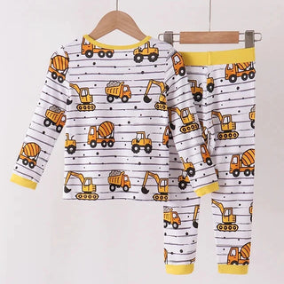 A two-piece boy pajama set hanging on wooden hangers against a plain white wall. The set includes a long-sleeve top and matching pants with a white background, black horizontal stripes, and a playful print of yellow construction vehicles including excavators, dump trucks, and cement mixers.