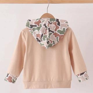 A children's hoodie shown from the back, hanging on a wooden hanger. The hoodie is a light peach-beige color with a camouflage pattern hood lining and matching camouflage-patterned cuffs.