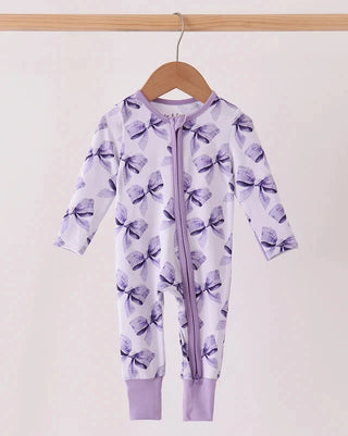 A baby long-sleeve footless zip-up sleeper in light lavender with a purple bow pattern, hanging on a wooden hanger against a plain light background.
