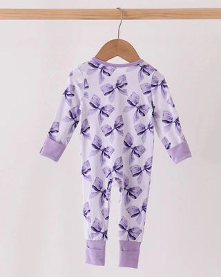 A baby long-sleeve footless jumpsuit hanging on a wooden hanger, featuring a purple bow pattern on a white background with lavender cuffs and hem.